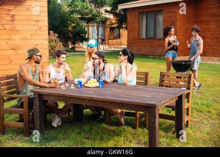 Gruppo di sorridere giovani amici seduti e parlare su outdoor summer party Foto Stock