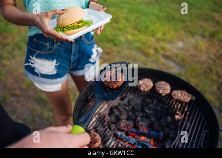 Vista superiore dei giovani la cottura di incontrare sul barbeque e rendendo hamburger all'aperto Foto Stock