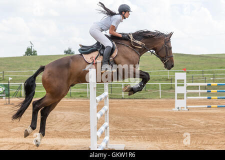 Vista laterale di bellissimi capelli lunghi horsewoman saltando su un cavallo marrone Foto Stock