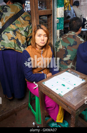 Local giovane ragazza in una fase di stallo la presentazione e la vendita di qualità gemma verde giada al Mercato della Giada, Mandalay Myanmar (Birmania) Foto Stock