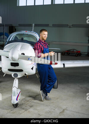 Felice giovane uomo in uniforme in piedi in aereo in hangar Foto Stock