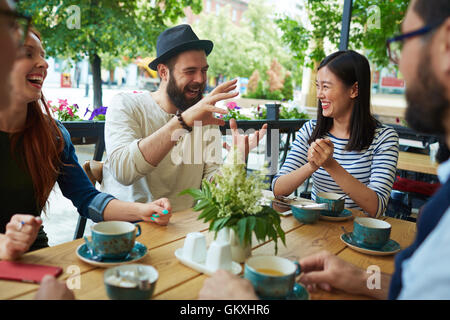 Uomo Barbuto in hat dicendo ai suoi amici storia divertente in cafe Foto Stock