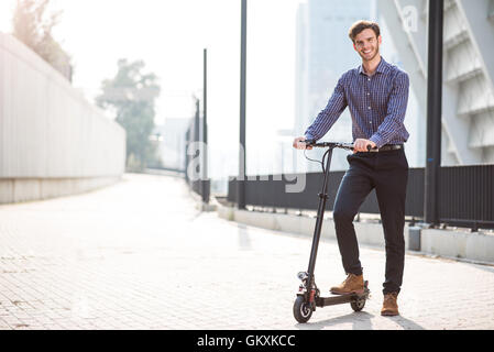 Piacevole uomo sorridente a cavallo di un kick scooter Foto Stock