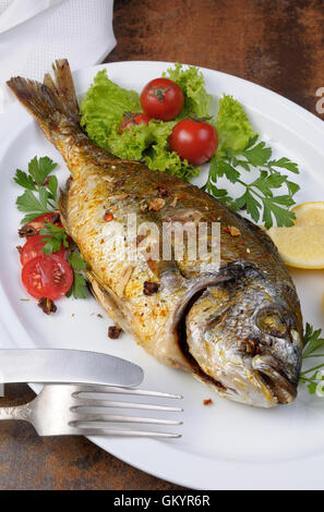 Pesce arrosto Dorado con verdure guarnire e le fette di limone su una piastra Foto Stock