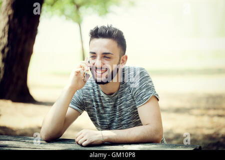 Giovane uomo presso il parco utilizza lo smartphone in una giornata di sole. Foto Stock