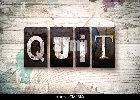 La parola 'quit' scritto in vintage metallo sporchi tipo di stampa in rilievo su un dipinto di bianco sullo sfondo di legno con inchiostro e macchie di vernice. Foto Stock