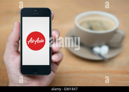 Un uomo guarda al suo iPhone che visualizza la Air Asia logo, mentre sat con una tazza di caffè (solo uso editoriale). Foto Stock