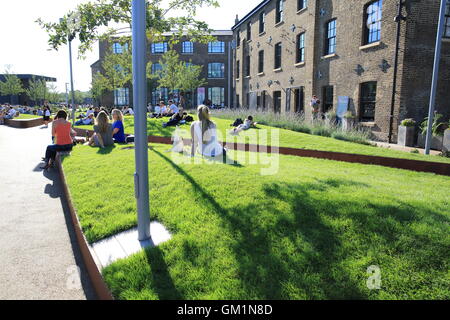 Persone rilassante sull'erba su Wharf Road, vicino a Piazza Granaio, in Kings Cross area di rigenerazione, a Londra NC1, Inghilterra Foto Stock