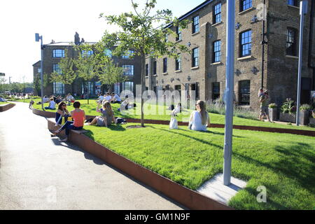 Persone rilassante sull'erba su Wharf Road, vicino a Piazza Granaio, in Kings Cross area di rigenerazione, a Londra NC1, Inghilterra Foto Stock