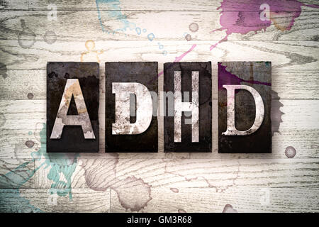 La parola "ADHD' scritto in vintage metallo sporchi tipo di stampa in rilievo su un dipinto di bianco sullo sfondo di legno con inchiostro e macchie di vernice. Foto Stock