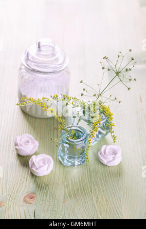 Giallo fiori selvatici in piccoli flaconi di vetro su una luce tavolo in legno Foto Stock