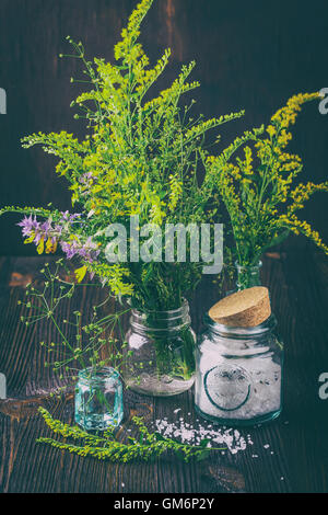 Giallo e viola fiori selvatici in piccole bottiglie di vetro e di vasi con cosmetici sale su una tavola di legno Foto Stock