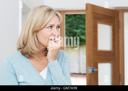 Triste donna matura che soffrono di agorafobia guardando fuori della porta aperta Foto Stock