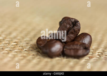 Tutto il caffè in grani impilati su una pianura Hessian sack. Foto Stock