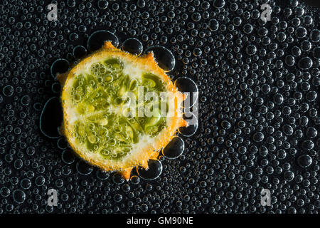 Kiwano, cornuto frutto di melone in acqua minerale, una serie di foto. Close-up di acqua gassata su sfondo nero Foto Stock