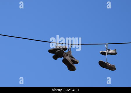 Calzatura tossing vecchio sneakers calzature con lacci delle scarpe legati appeso a un filo. Foto Stock