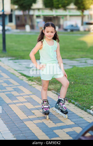 Poco Pretty girl su pattini a rotelle presso un parco Foto Stock