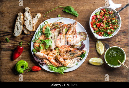 Piatto di pesce arrosto con fresco porro, insalata verde, peperoni, limone, pane, pesto su sfondo di legno, vista dall'alto Foto Stock