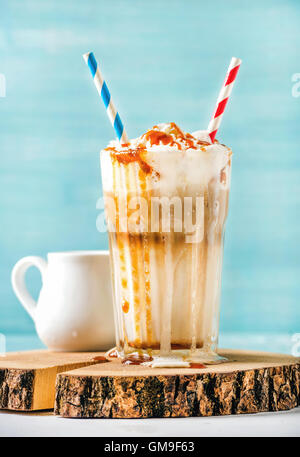 Latte macchiato con panna montata e salsa di caramello in bicchiere alto sulla tavola di legno blu sulla parete dipinta sullo sfondo Foto Stock