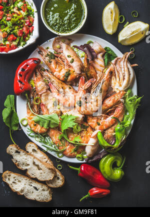 Piatto di gamberoni tigre arrostiti e pezzi di polipo con porri freschi, insalata, peperoni, limone, pane, pesto su sfondo nero Foto Stock