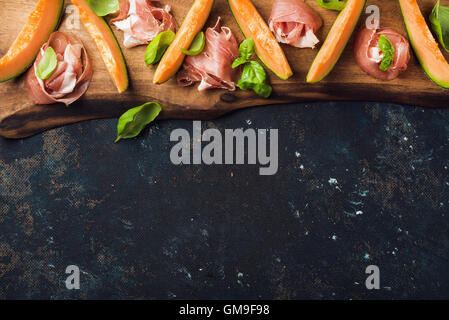 Il Prosciutto con il melone Cantalupo e le foglie di basilico sul pannello di legno Foto Stock