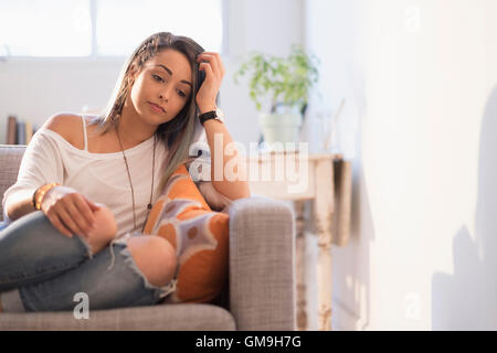 Triste giovane donna seduta su un divano Foto Stock
