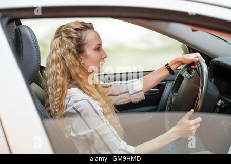 Donna con ricci, lunghi capelli biondi auto pilotaggio Foto Stock