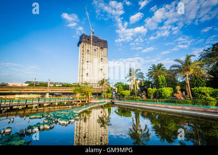 Stagno a Rizal Park e il grattacielo in costruzione, in Ermita, Manila, Filippine. Foto Stock