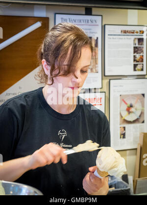 Un lavoratore dei mestieri con cautela un caramello salato gelato presso la famosa gelateria Bella di Coal Harbour, Vancouver, BC, Canada. Foto Stock