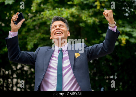 Gioioso uomo d'affari con pelle d'oliva con le braccia sollevate e tenendo il telefono cellulare in una mano. Foto Stock