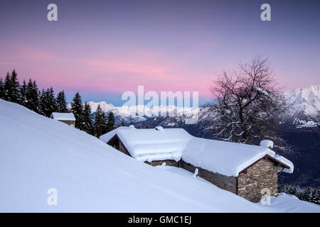 Cielo rosa all'alba sopra coperta di neve di capanne e alberi tagliate di sopra di Gerola Alta Valtellina Alpi Orobie Lombardia Italia Europa Foto Stock