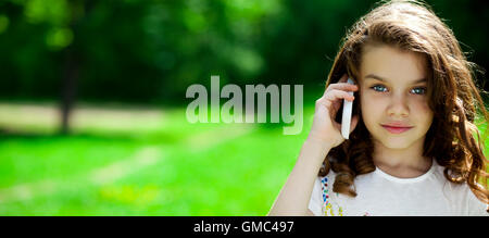 Bellissima bambina chiamando dal telefono cellulare sullo sfondo del parco di estate Foto Stock