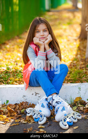 Ritratto di una decina di anni di ragazza siede su un parco giochi in pattini a rotelle Foto Stock