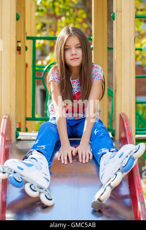 Ritratto di una decina di anni di ragazza siede su un parco giochi in pattini a rotelle Foto Stock