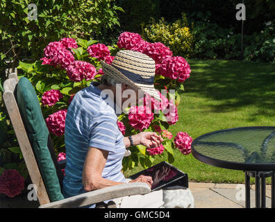 Signora matura nel cappello per il sole seduti fuori in un giardino utilizzando un iPad, REGNO UNITO Foto Stock