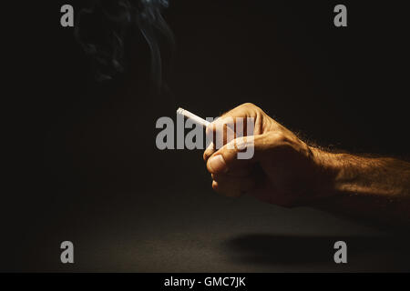 Composizione concettuale sul fumo, studio shot di una mano di un uomo in possesso di un sigaro. Foto Stock