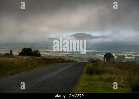 Ingleborough incombente fuori della nebbia e cloud da un strada tranquilla nella foresta di Bowland, Yorkshire Dales, REGNO UNITO Foto Stock