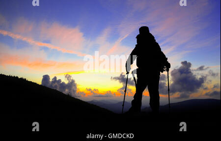 Escursionista silhouette con zaino e bastoncini da trekking sul picco di montagna ammirando il tramonto Foto Stock