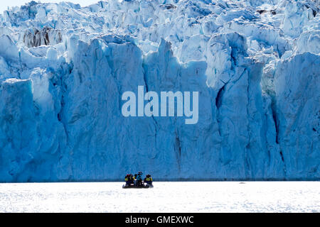 Il gigantesco frontale del ghiacciaio Rijpbreen in Svalbard con un gruppo di turisti su un zodiac ammirando la scala di esso. Foto Stock