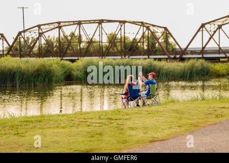 Una giovane coppia caucasica si diverte a pescare sulla costa del fiume canadese settentrionale vicino al ponte in acciaio del lago Overholser. Oklahoma, USA. Foto Stock