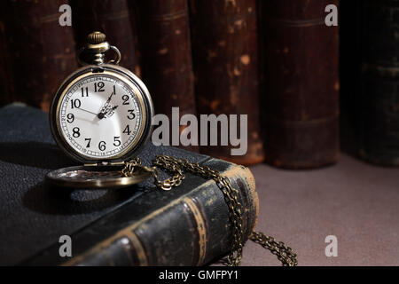 Libreria vintage. Vintage orologio da tasca in prossimità dei libri in una fila su sfondo scuro Foto Stock