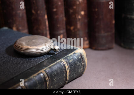 Libreria vintage. Argento vecchio orologio da tasca in prossimità dei libri in una fila su sfondo scuro Foto Stock