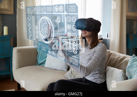 La donna si siede sul divano di casa indossando la realtà virtuale auricolare Foto Stock