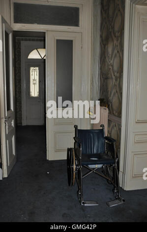 Sedia a rotelle vintage e porte di vetro in casa abbandonata. Foto Stock