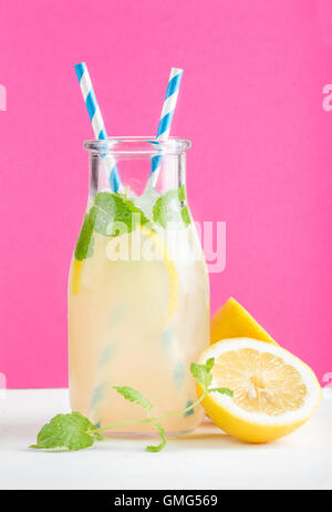 Bottiglia di limonata fatta in casa con la menta, ghiaccio, limoni, carta cannucce e luminoso sfondo viola Foto Stock