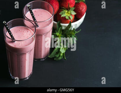 Fragola e menta frullato in bicchieri alti, bawl dei frutti di bosco freschi in scuro legno rustico sfondo Foto Stock