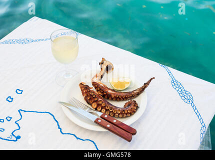 Polpo alla brace e vino bianco vetro su di un tavolo presso la costa del mare Foto Stock