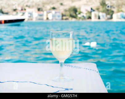 Bicchiere di vino bianco sul tavolo nel ristorante sulla spiaggia con vista sul mare, l'acqua è blu e yacht a sfondo Foto Stock