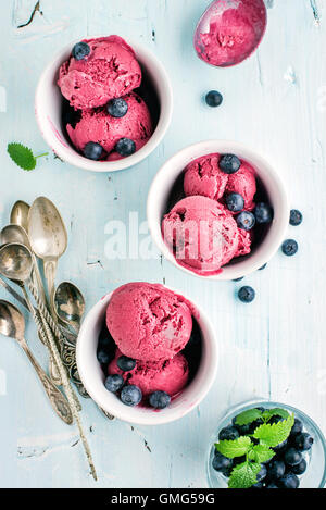 In casa mirtillo ice cream scoop con frutti di bosco freschi e le foglie di menta in tazze su fondo azzurro Foto Stock