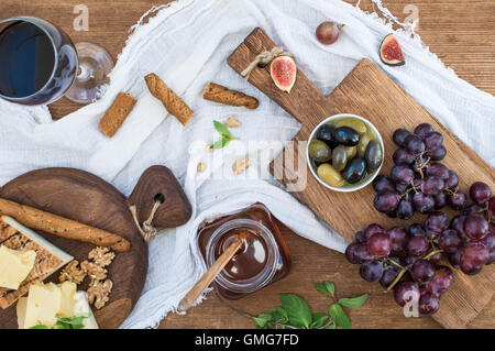 Bicchiere di vino rosso, formaggi, uva, noci, olive, miele e grissini Foto Stock
